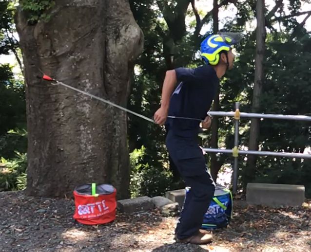 樹から離れた場所で、スローラインのウエイトを振って投げようとしている受講者の写真